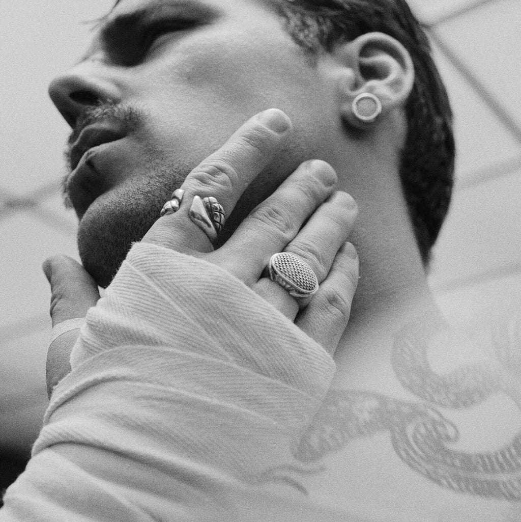 Close-up of a person with tattoos and jewelry, wearing a white garment.