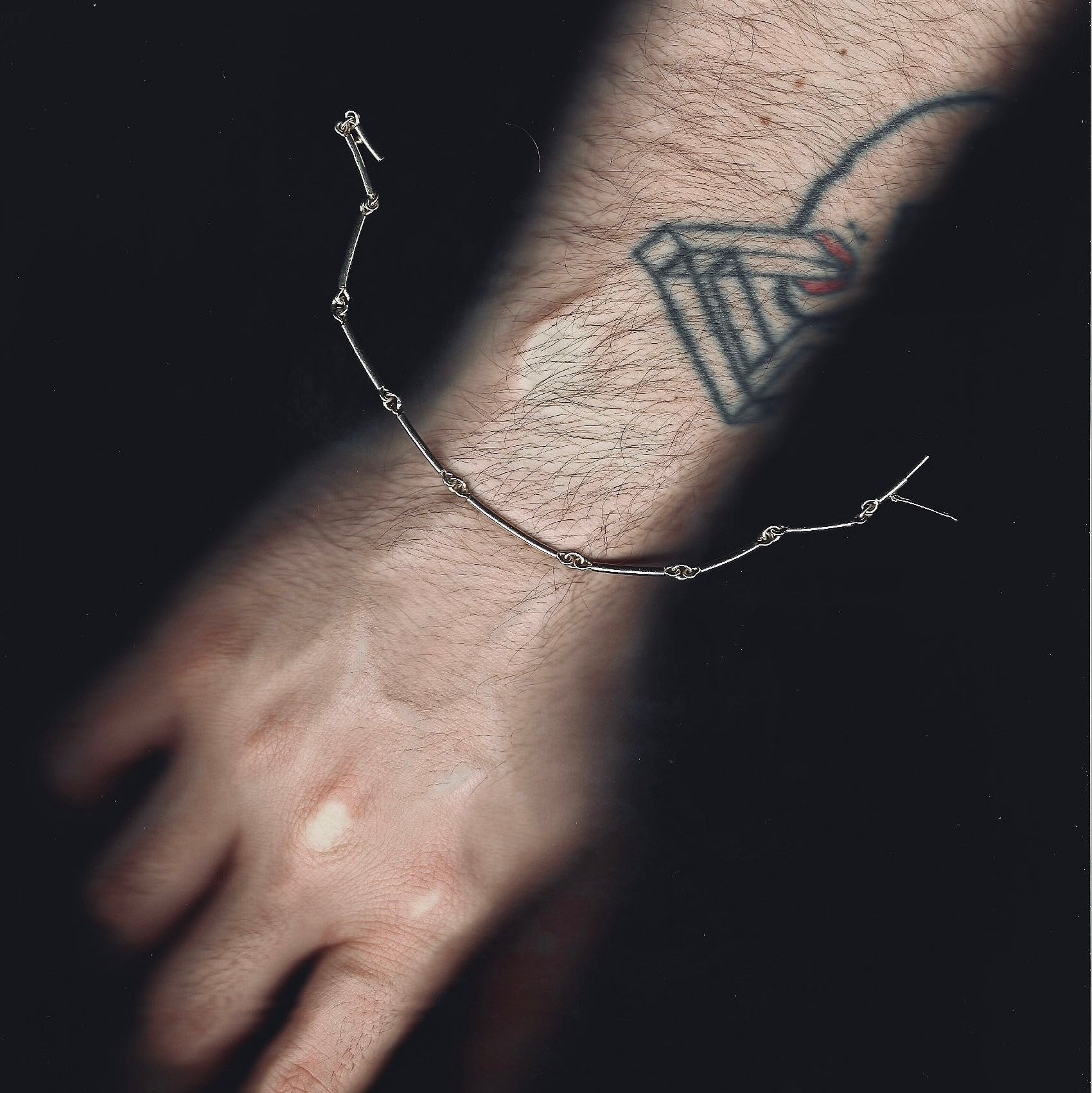 Close-up of a wrist with a bracelet and tattoo on a dark background