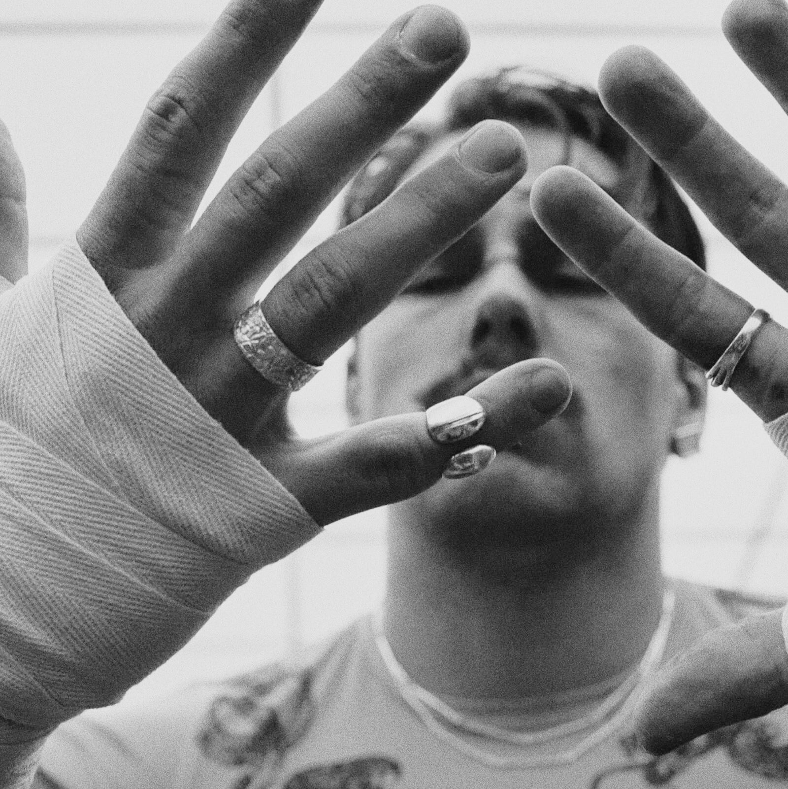 Person with tattooed hands covering their face, wearing a silver ring