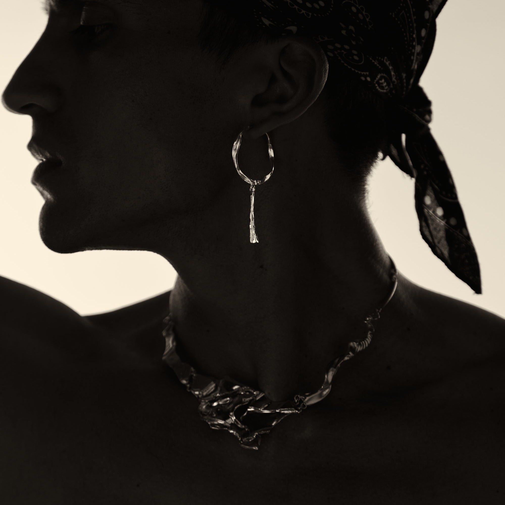 Silhouette of a person wearing hoop earrings and a bandana with a neutral background