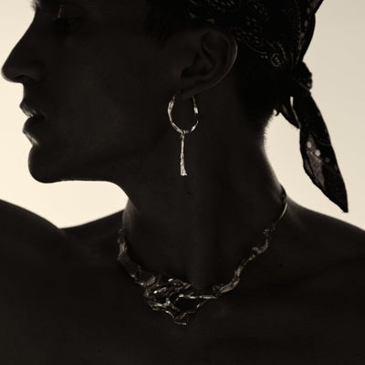 Silhouette of a person wearing hoop earrings and a bandana with a neutral background