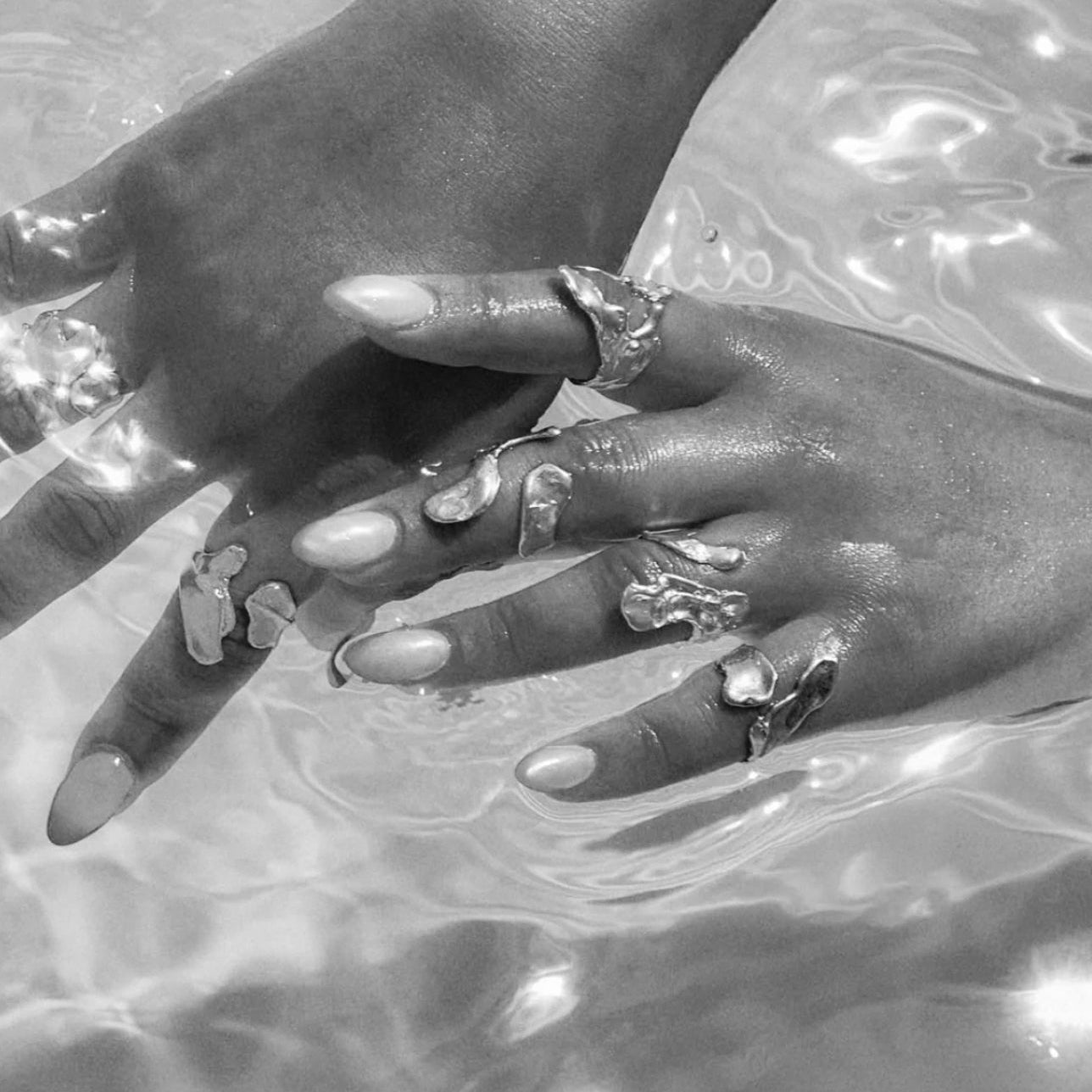 Close-up of hands with silver rings and nail polish against a reflective water background