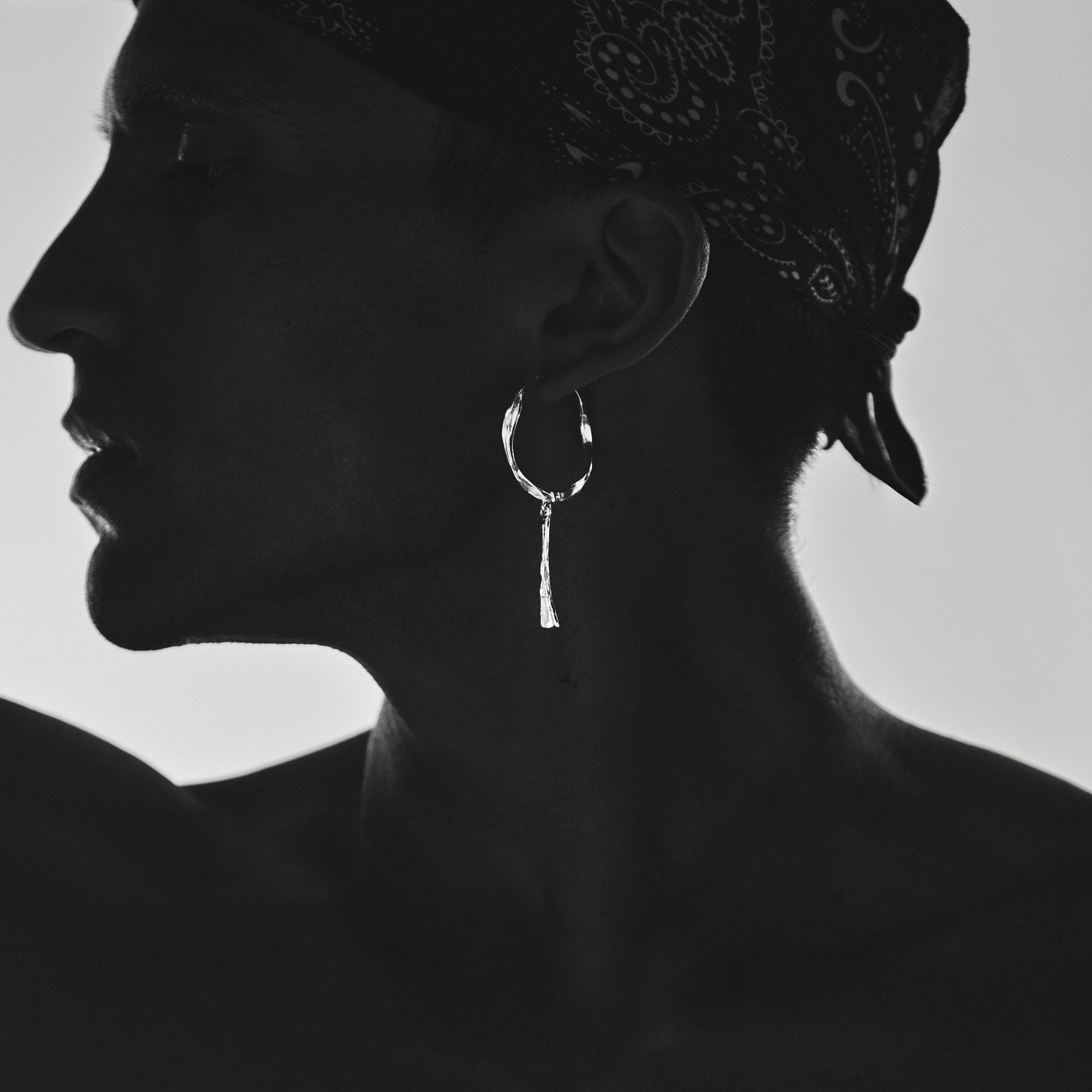Silhouette of a person wearing a bandana and Silver Bone hoop earrings on a plain background
