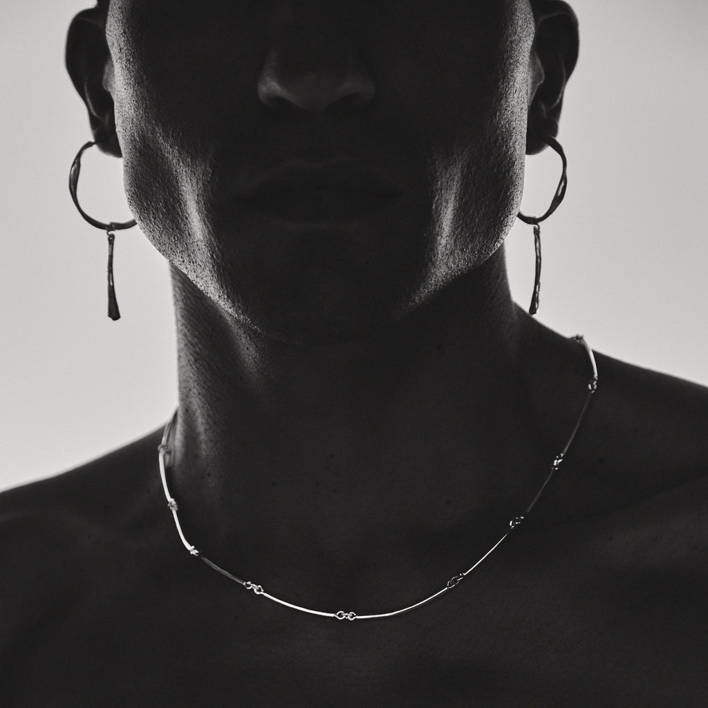 Person wearing hoop earrings and a delicate necklace against a neutral background