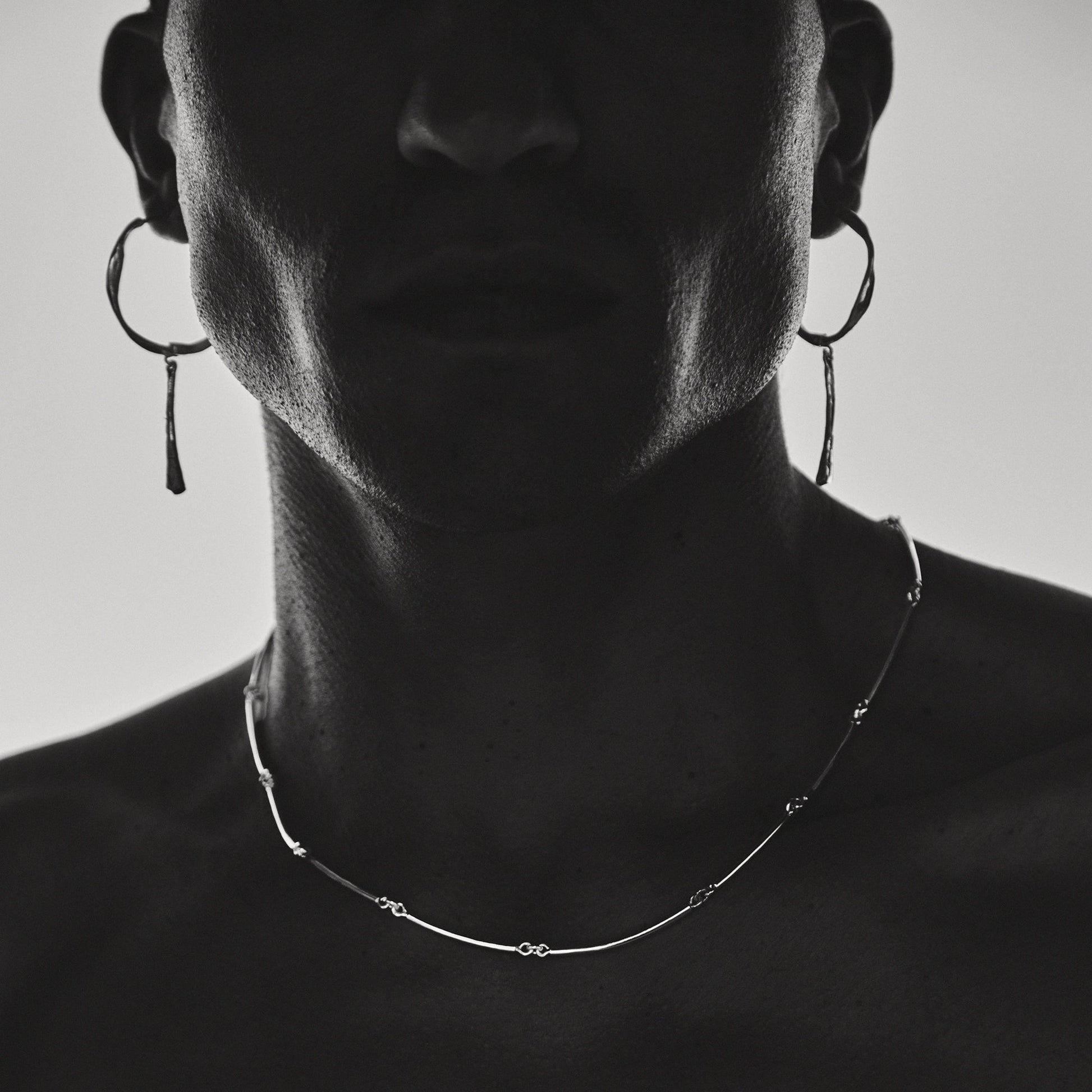 Person wearing hoop earrings and a delicate necklace against a neutral background