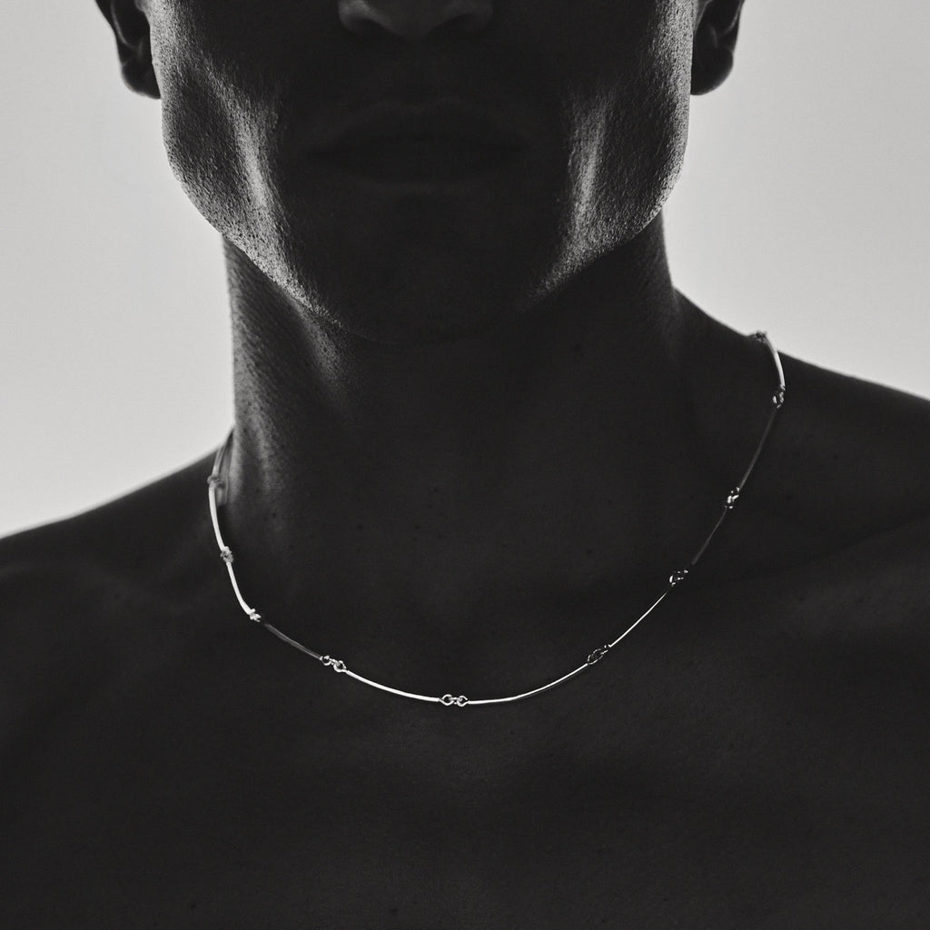 A man wearing a delicate necklace against a plain background