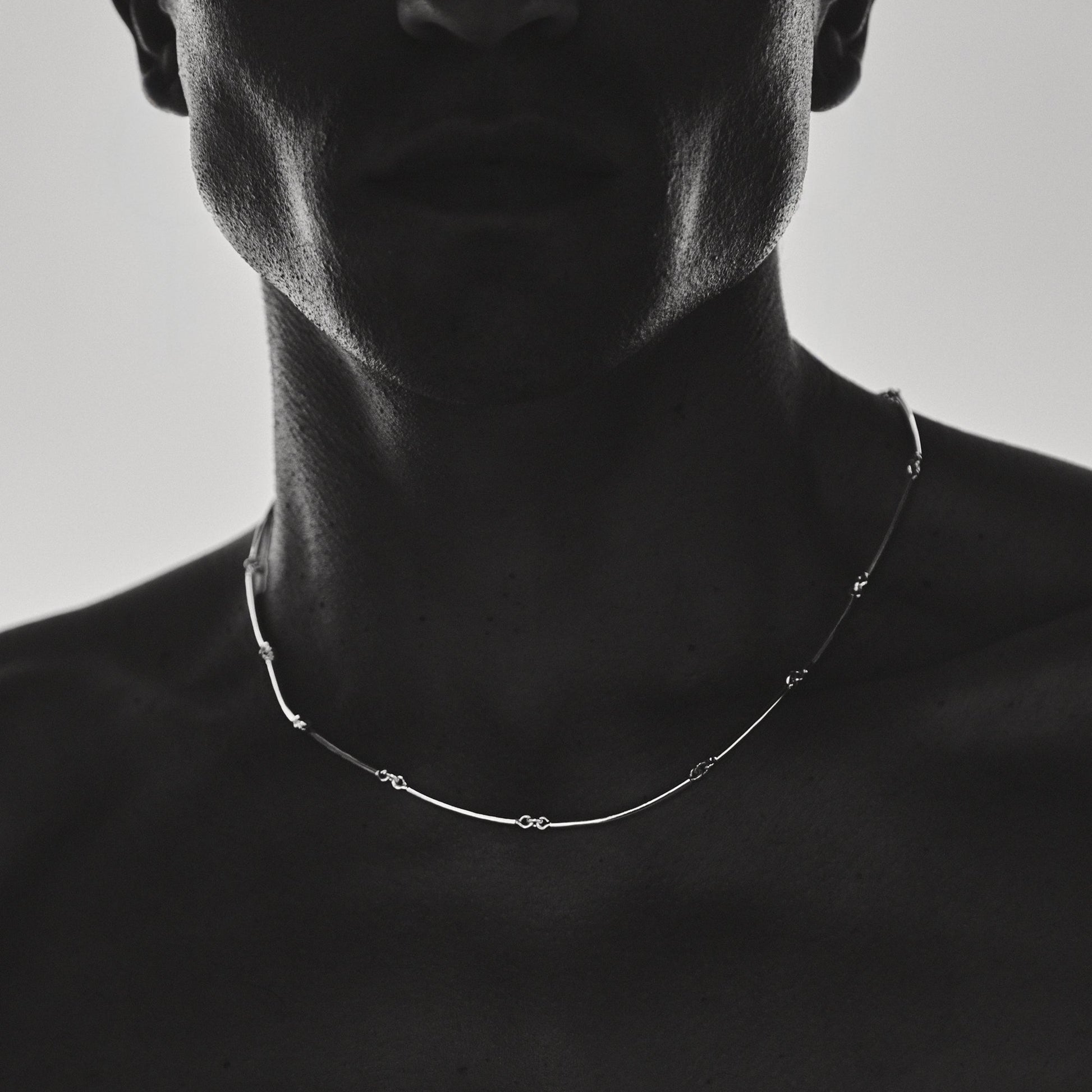 A man wearing a delicate necklace against a plain background