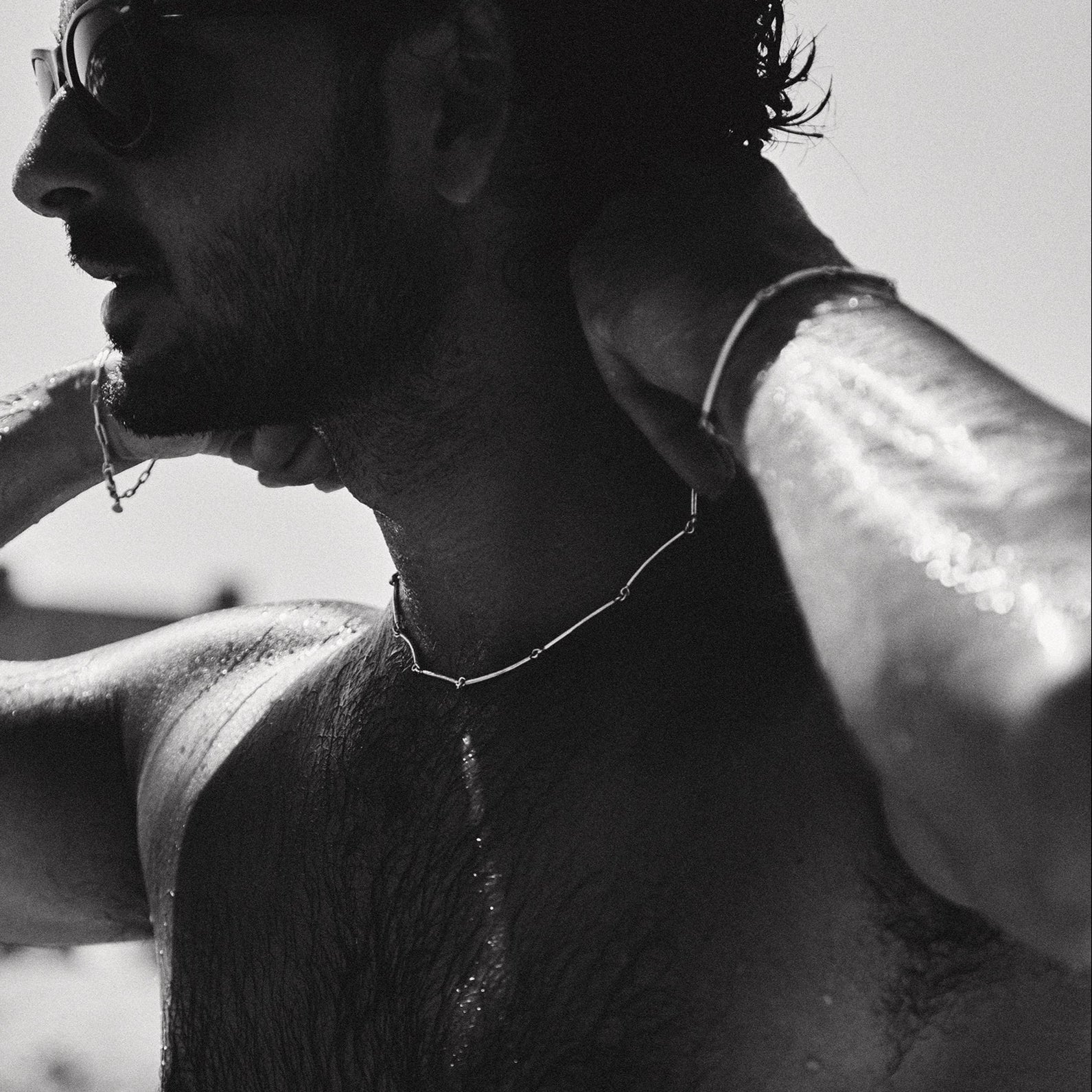 Black and white photo of a person with sunglasses and a necklace, possibly on a beach.