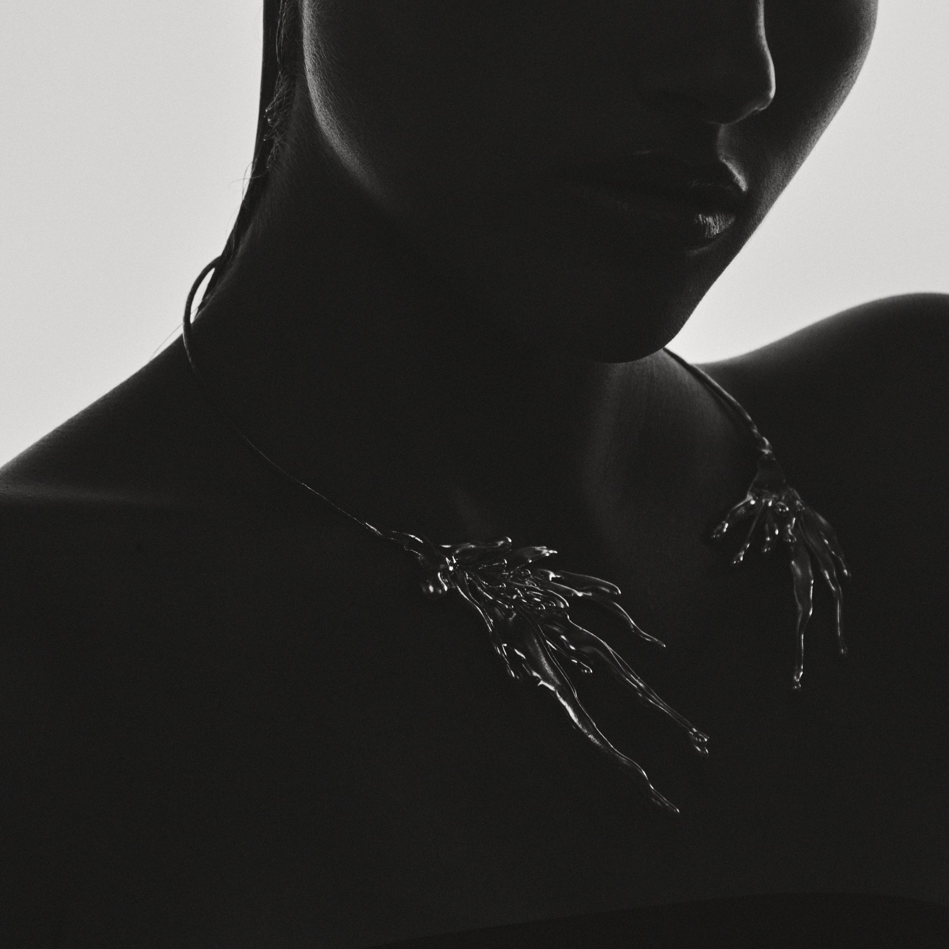 Silhouette of a person wearing a delicate necklace against a plain background