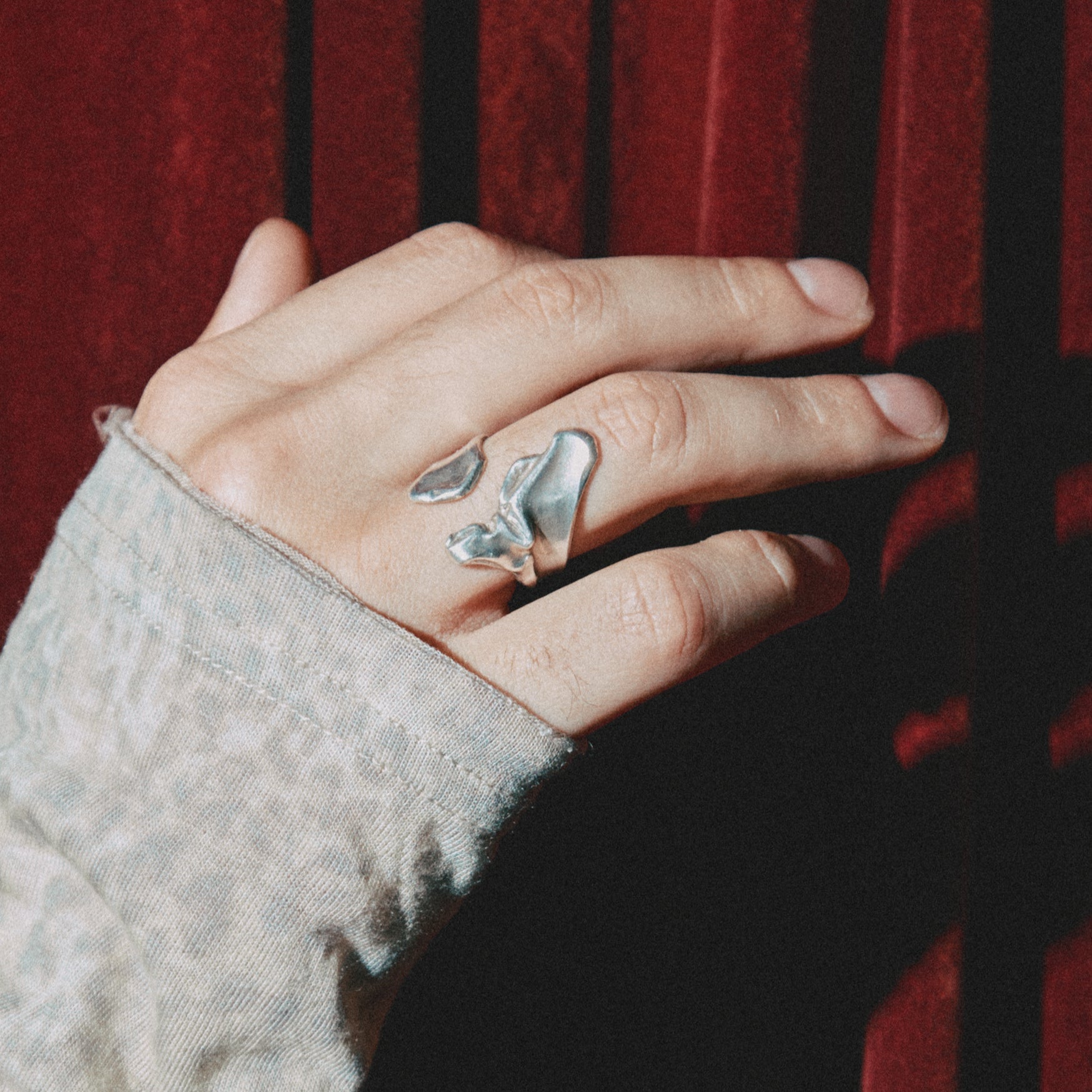Hand wearing a silver ring with leaf design against a red curtain background