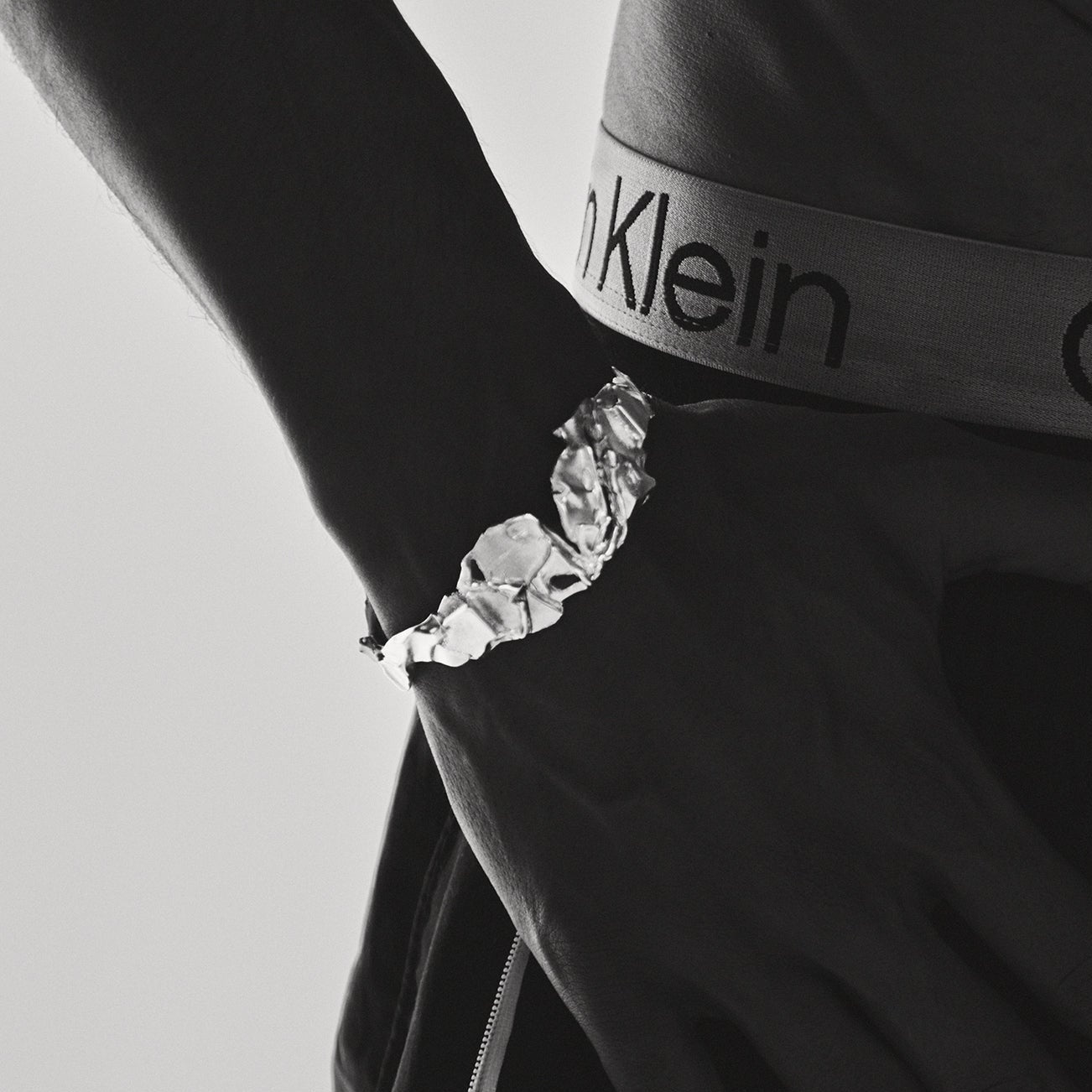 Close-up of a hand wearing a bracelet with a Calvin Klein logo on a black background