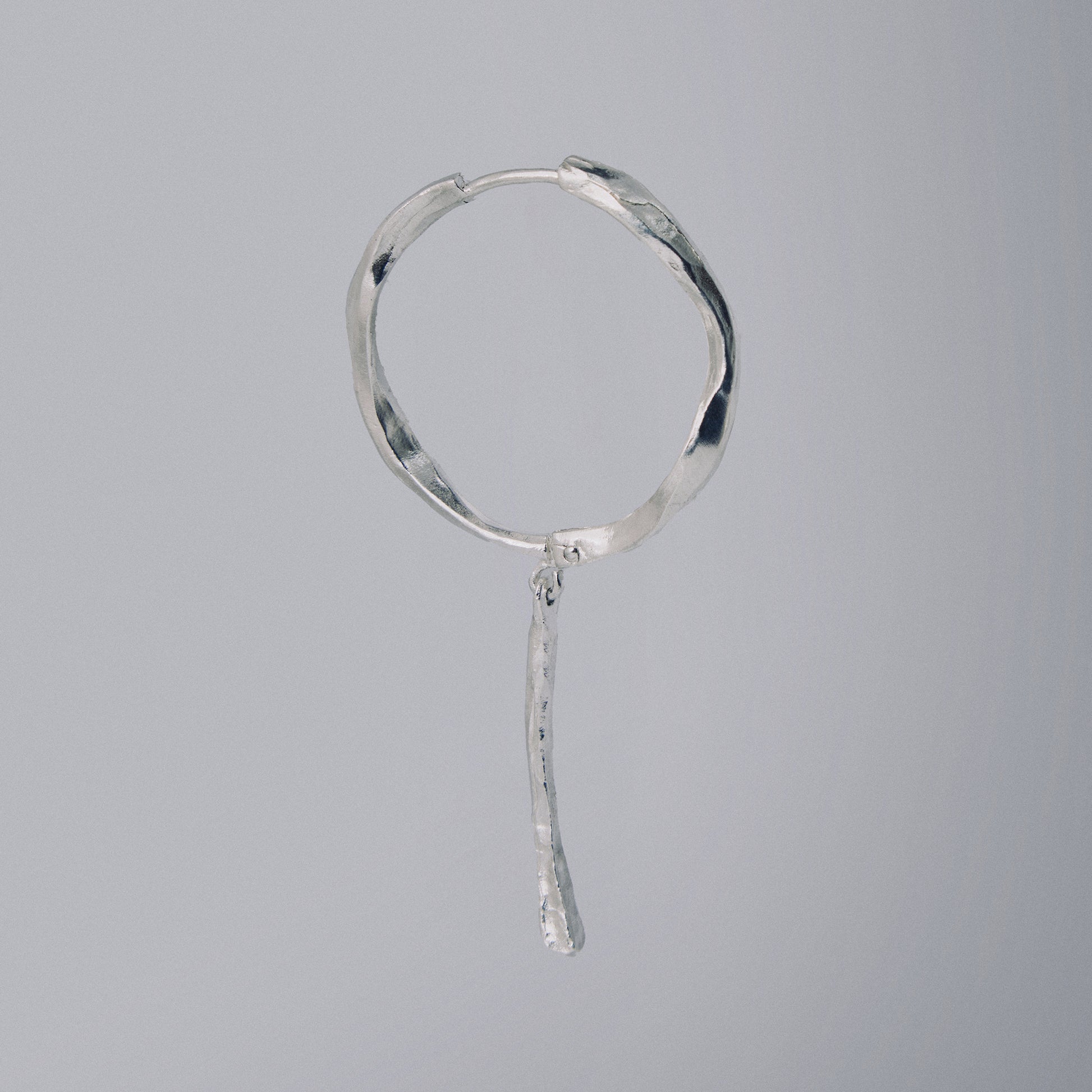 Silver hoop earring with a dangling element on a gray background