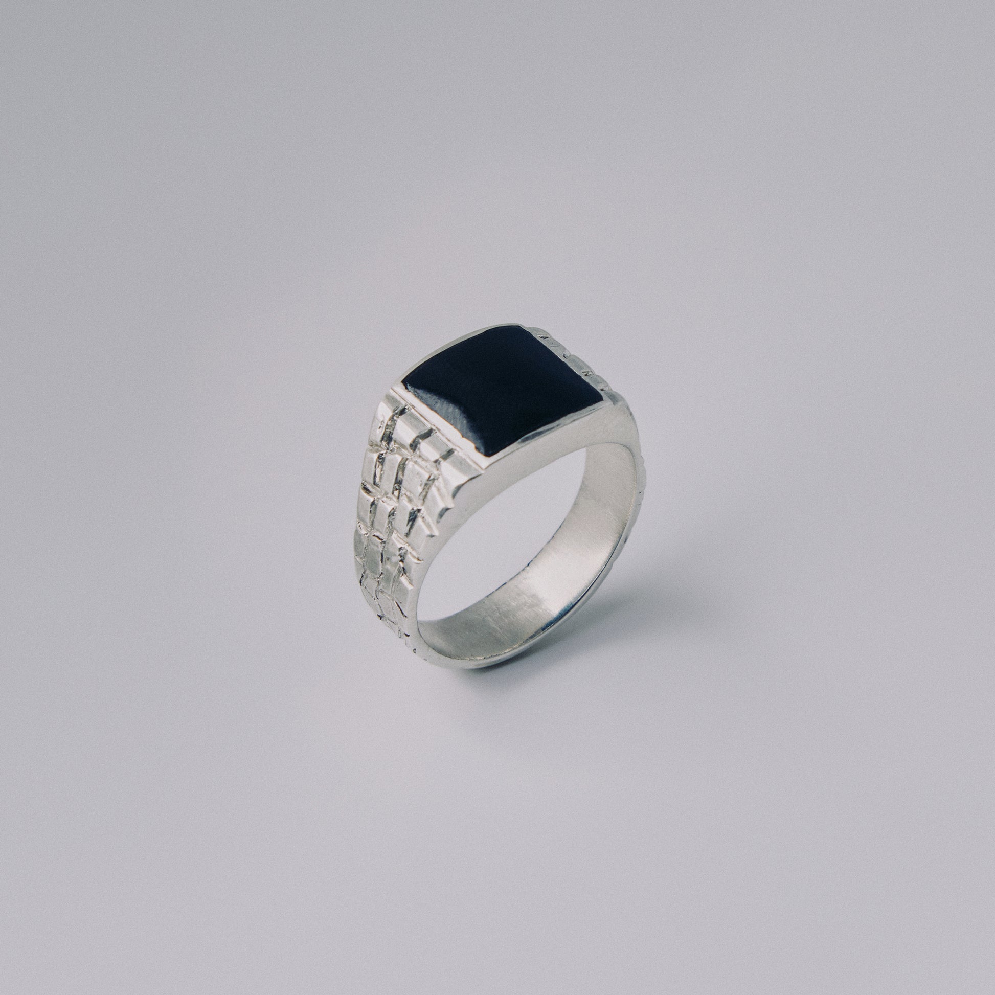 Silver ring with a black square stone on a gray background