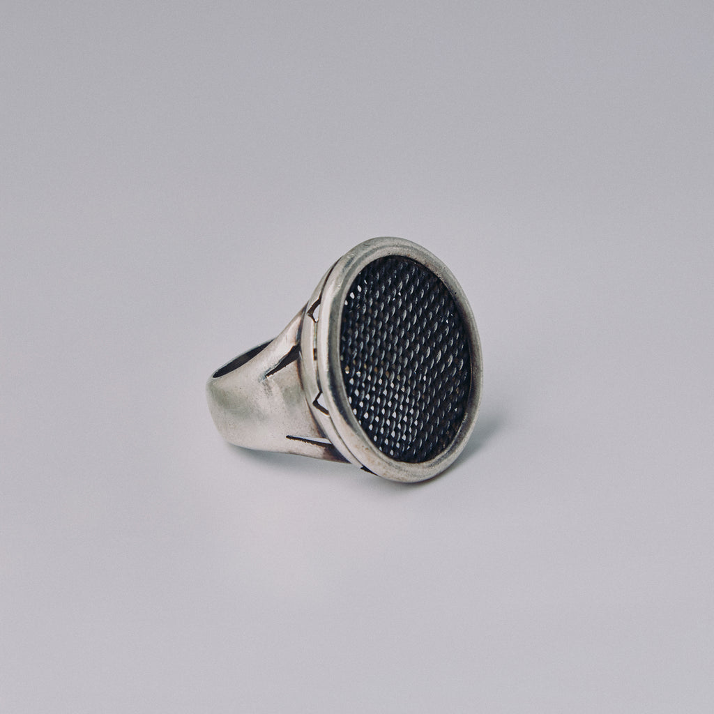 Silver ring with textured black center on a gray background