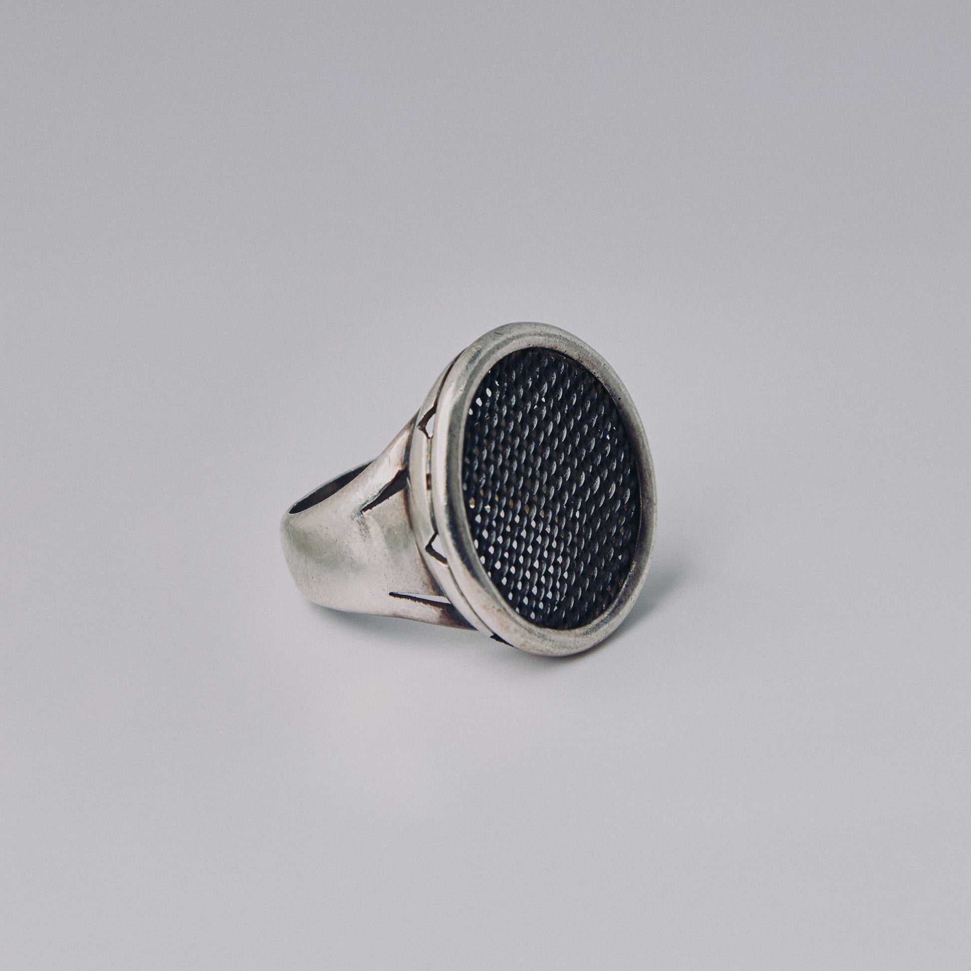 Silver ring with textured black center on a gray background