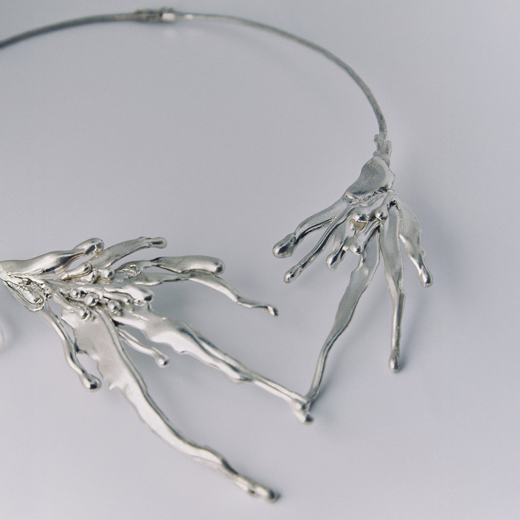 Silver branch-like necklace on a light gray background
