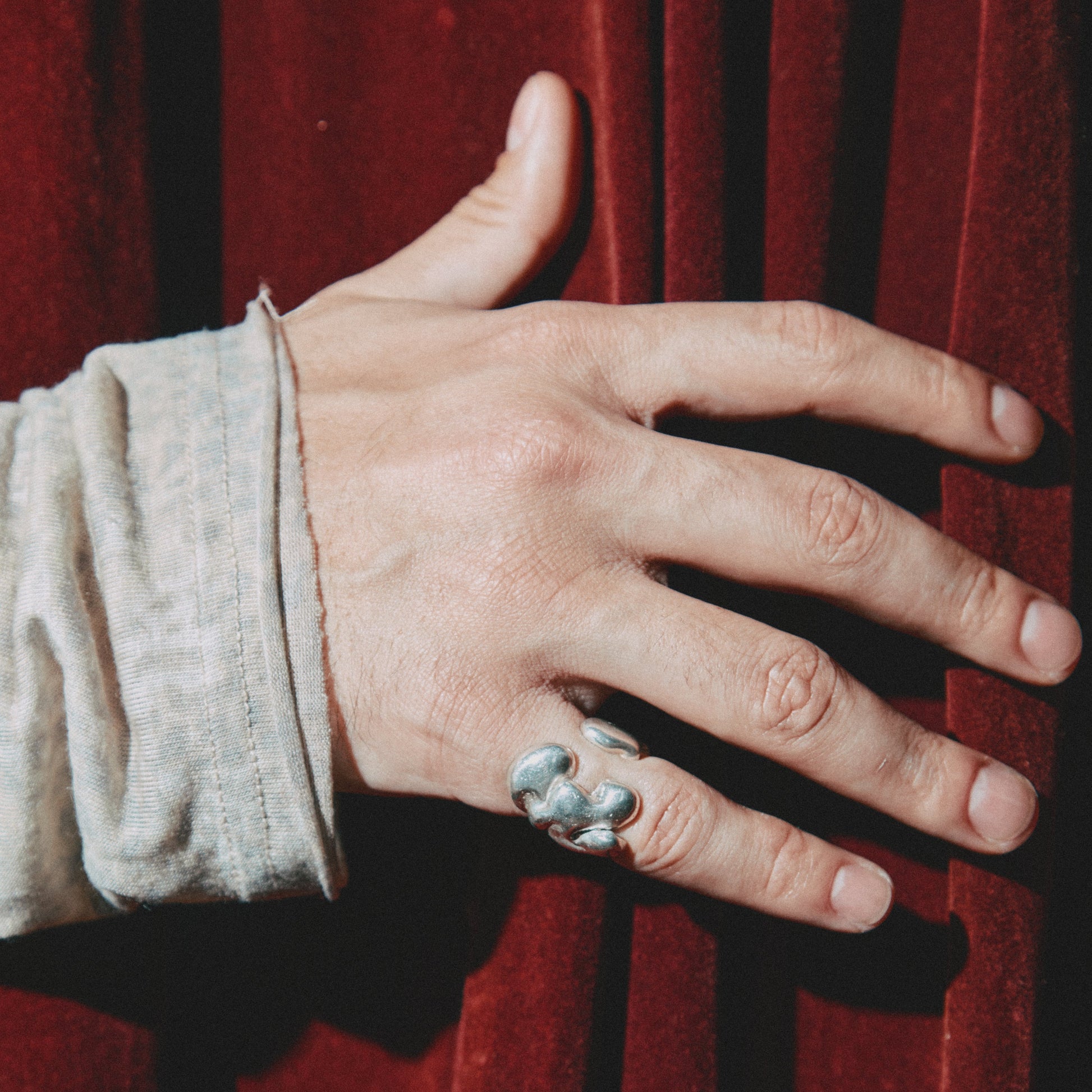 Hand wearing a silver ring on a red background