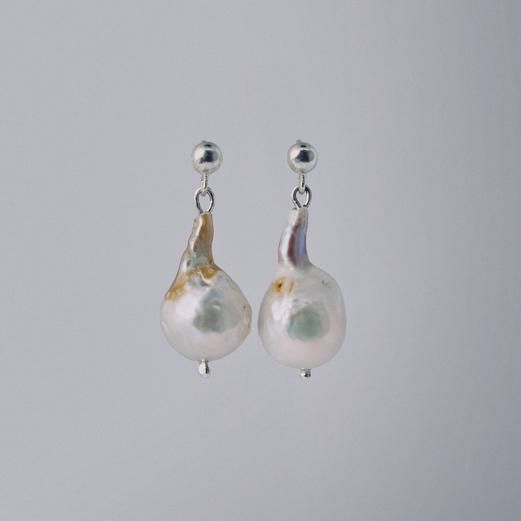 Pair of pearl earrings with silver hooks on a gray background