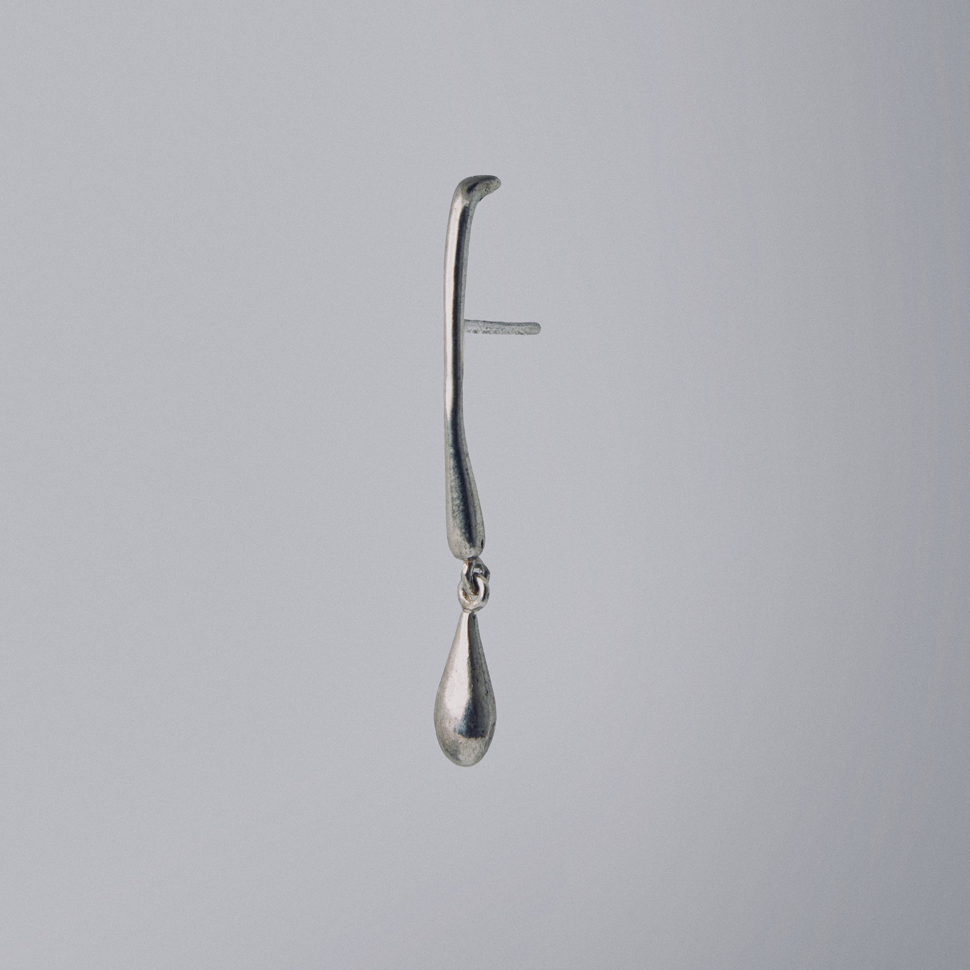 Silver earring with a teardrop design on a gray background