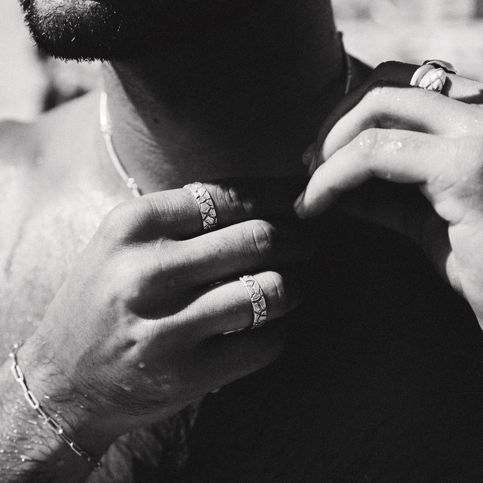 Close-up of a person's hands with rings on fingers, wearing a necklace.
