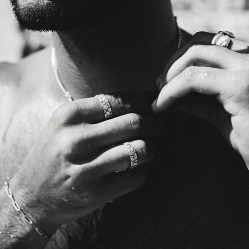 Close-up of a person's hands with rings on fingers, wearing a necklace.