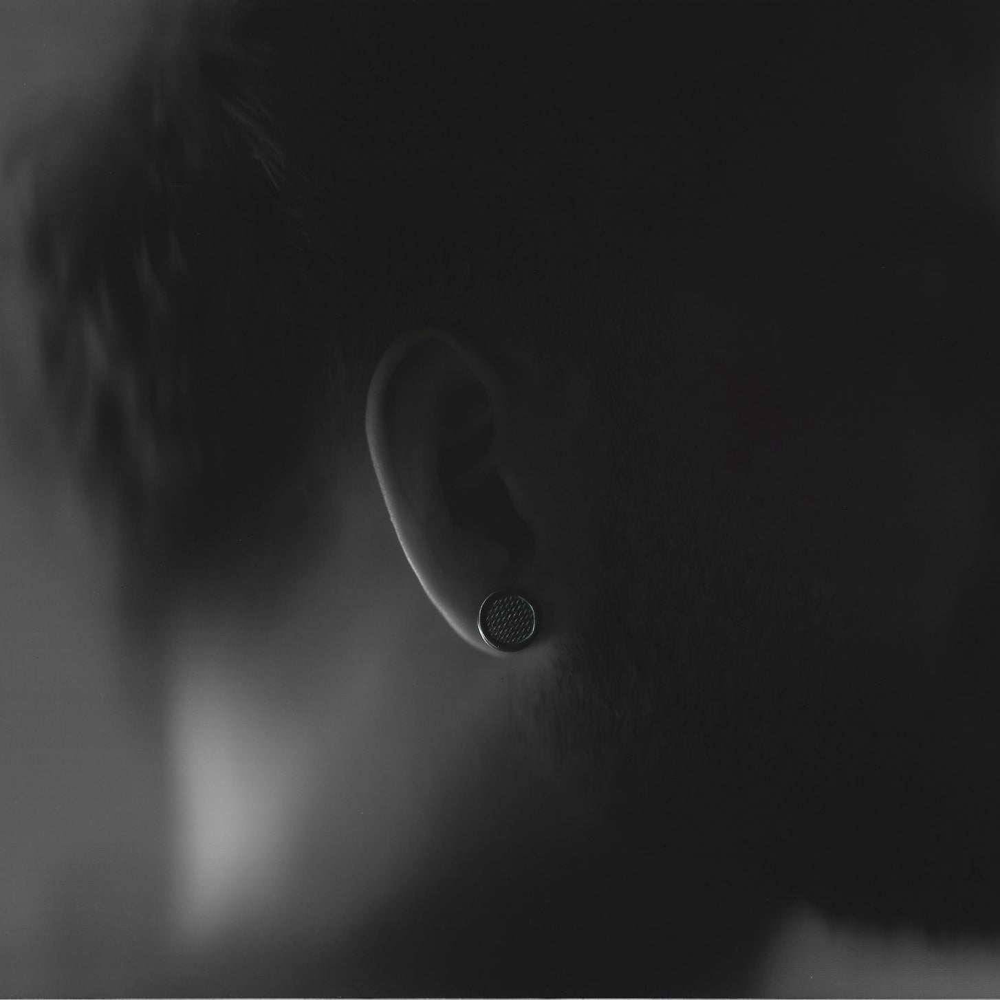 Close-up of an ear with a small round earring, blurred background