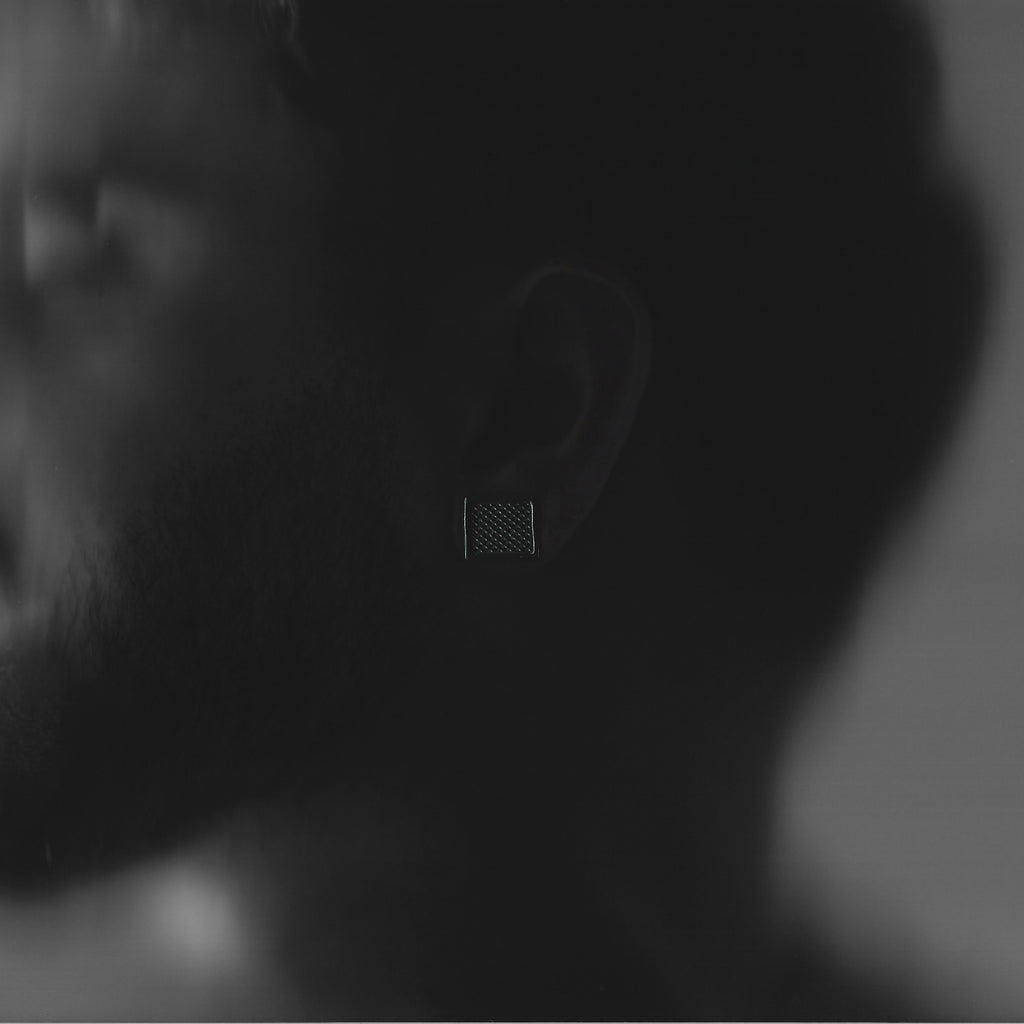 Close-up of a person wearing a square textured earring with a blurred background