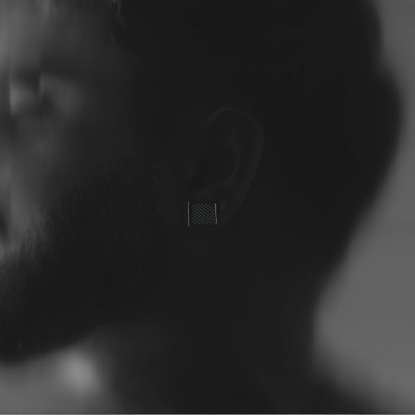 Close-up of a person wearing a square textured earring with a blurred background