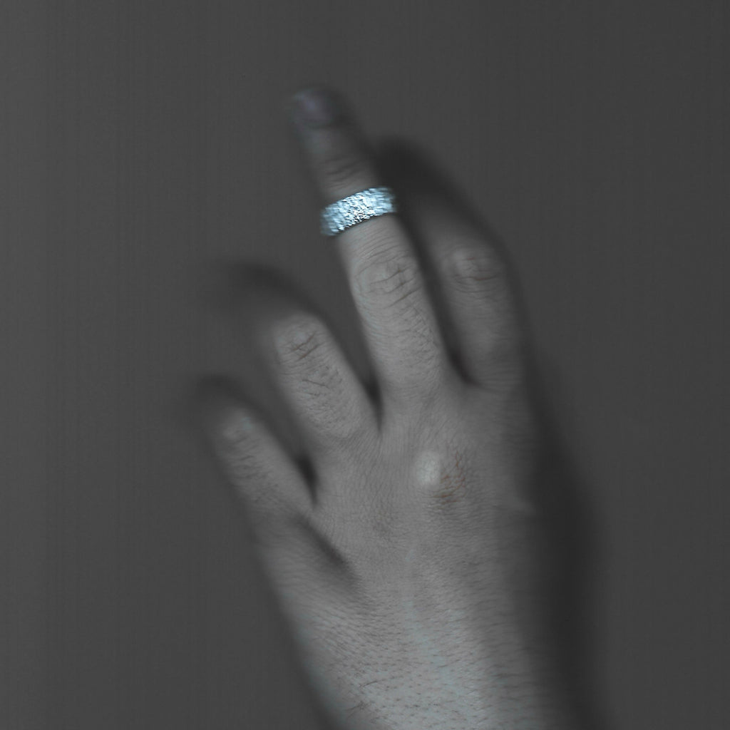 Hand wearing a silver ring on a dark background
