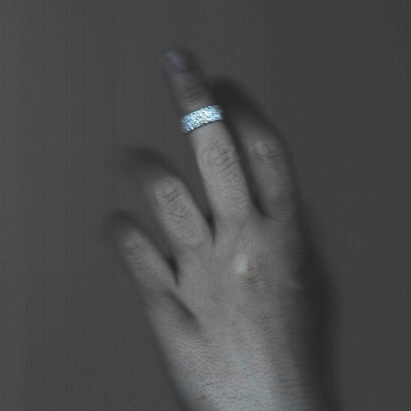 Hand wearing a silver ring on a dark background
