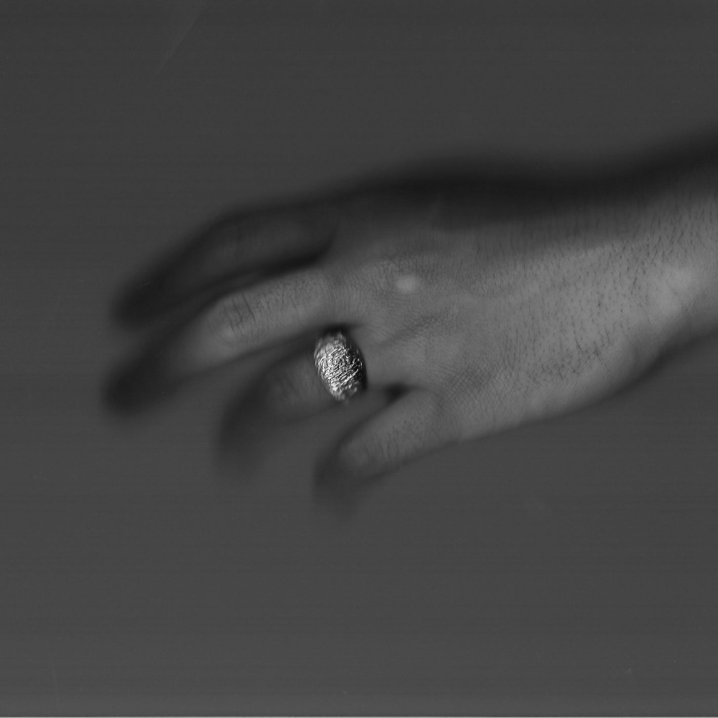 Close-up of a hand wearing a ring with a textured band on a dark background