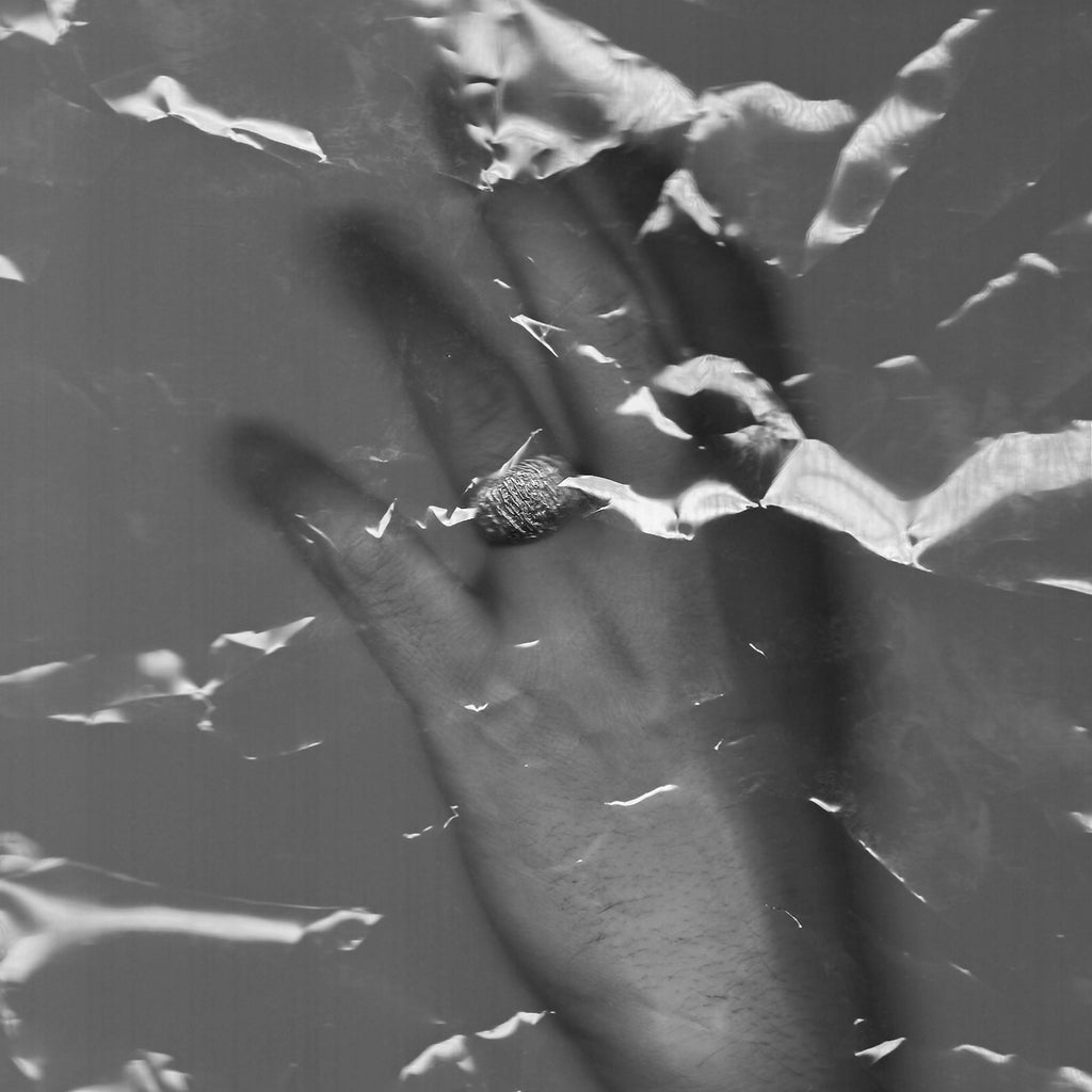Black and white image of a hand with a ring on a textured surface