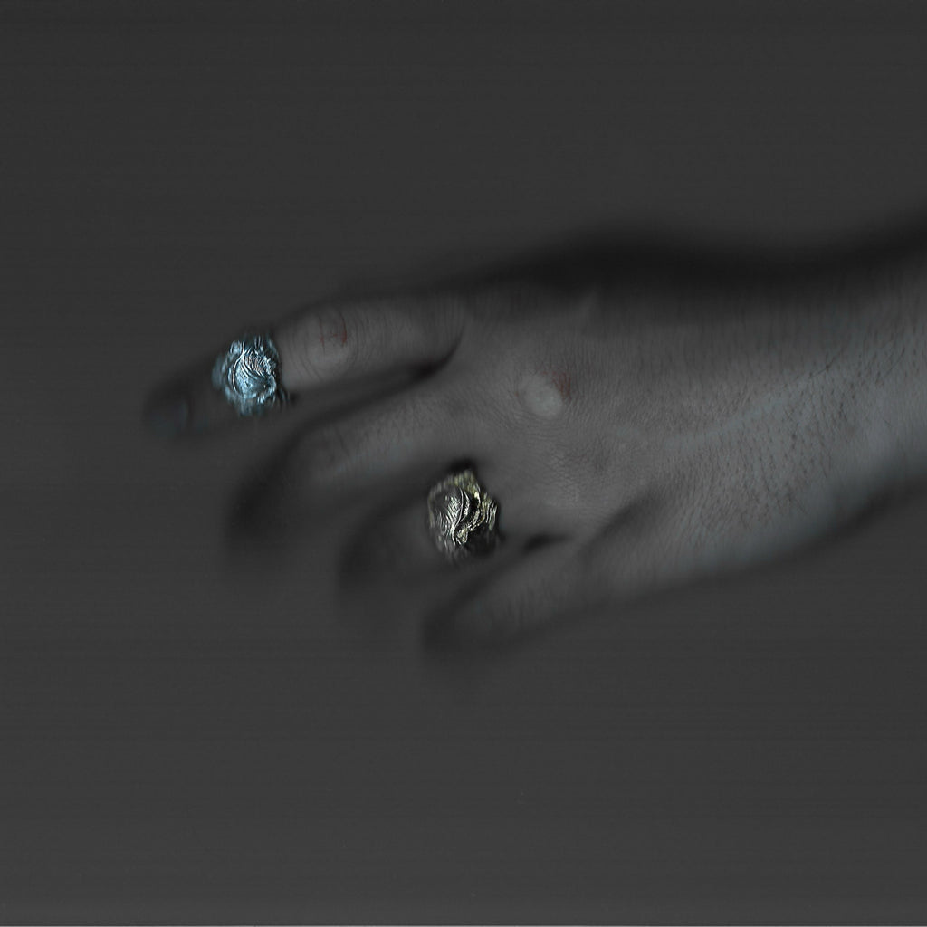 Close-up of a hand wearing two rings with blue and silver stones on a dark background