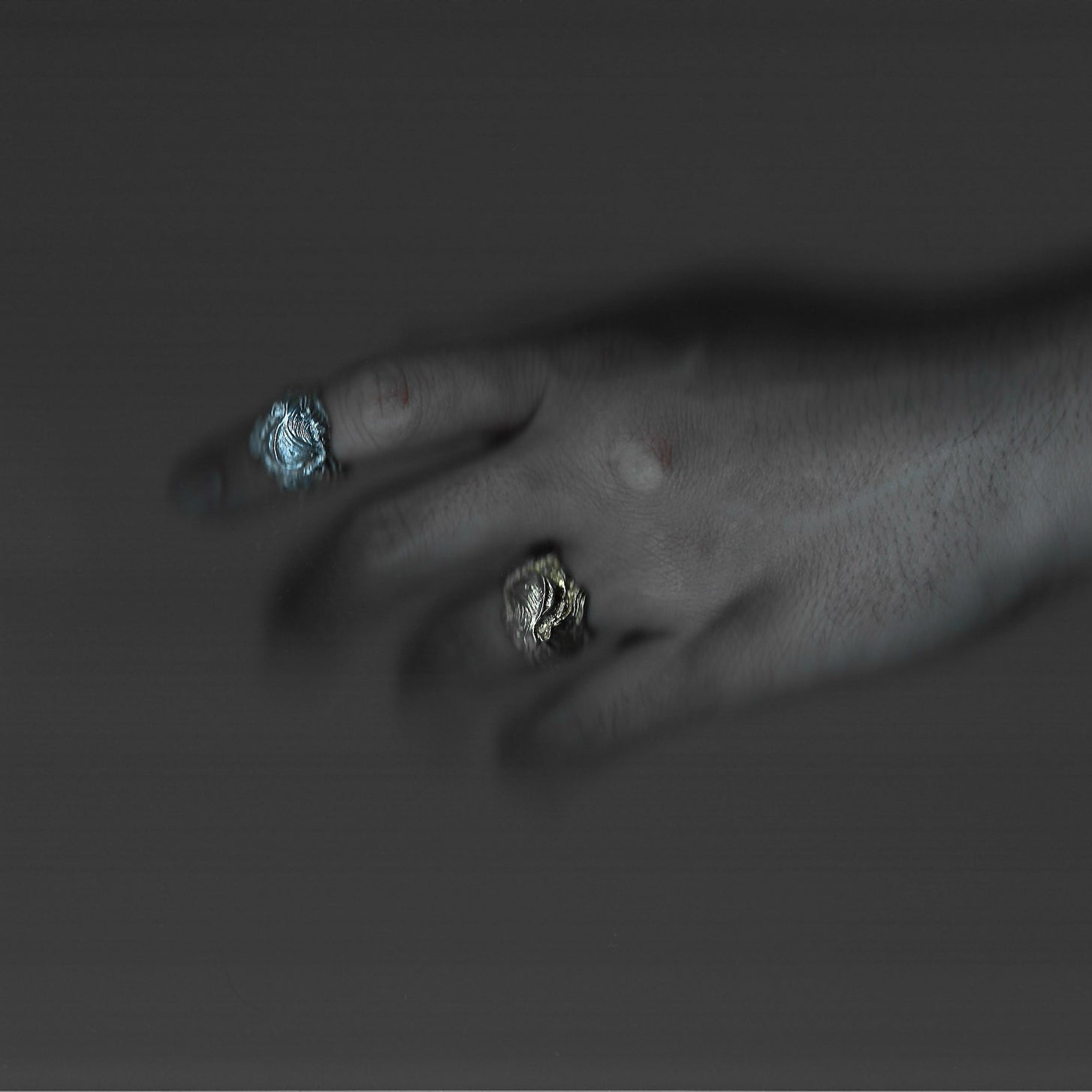 Close-up of a hand wearing two rings with blue and silver stones on a dark background
