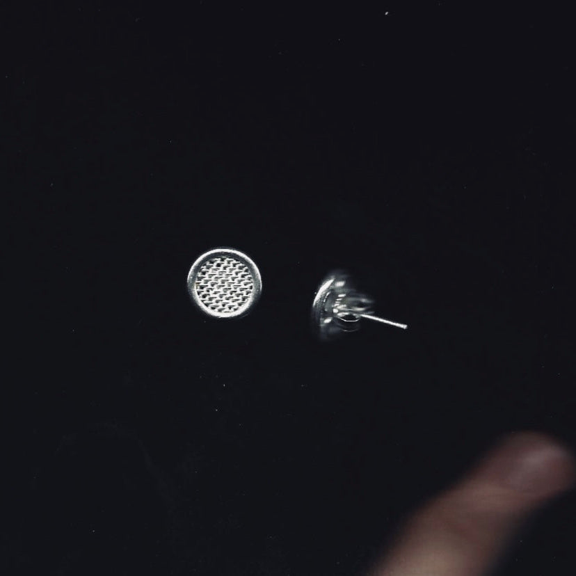 Silver earrings on a dark surface with a hand holding one earring.