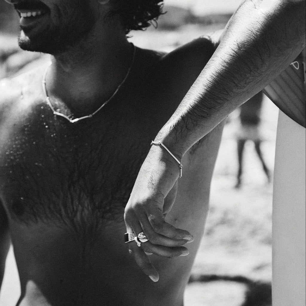 Black and white photo of a shirtless man with sunglasses on a beach.