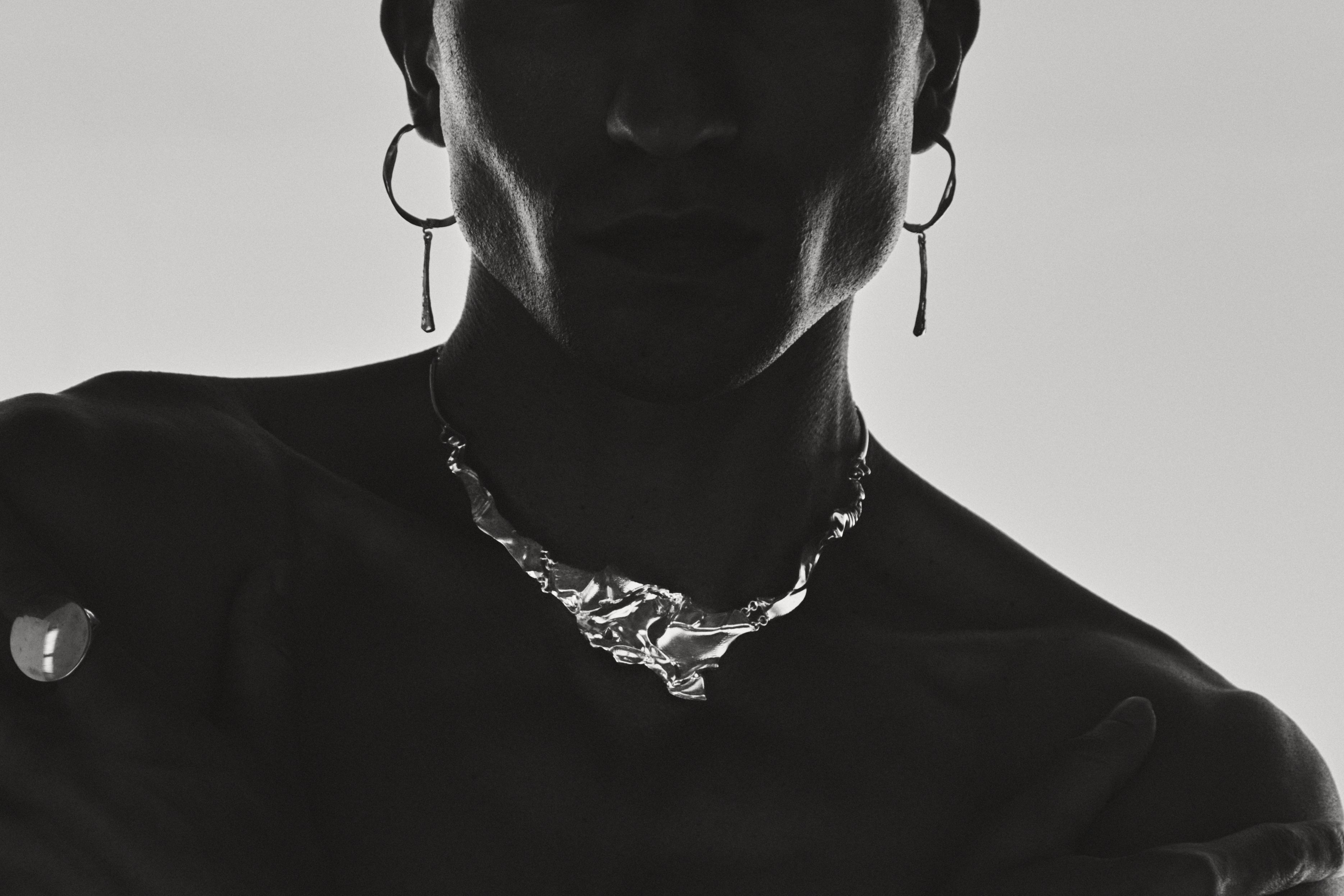 Black and white silhouette of a person wearing a necklace with a minimal background