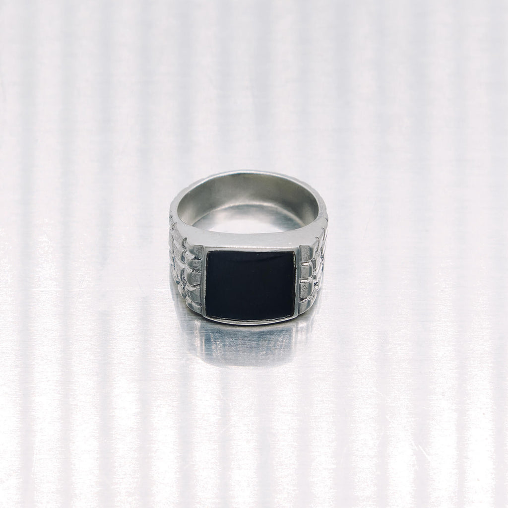 Silver ring with a black square stone on a white background