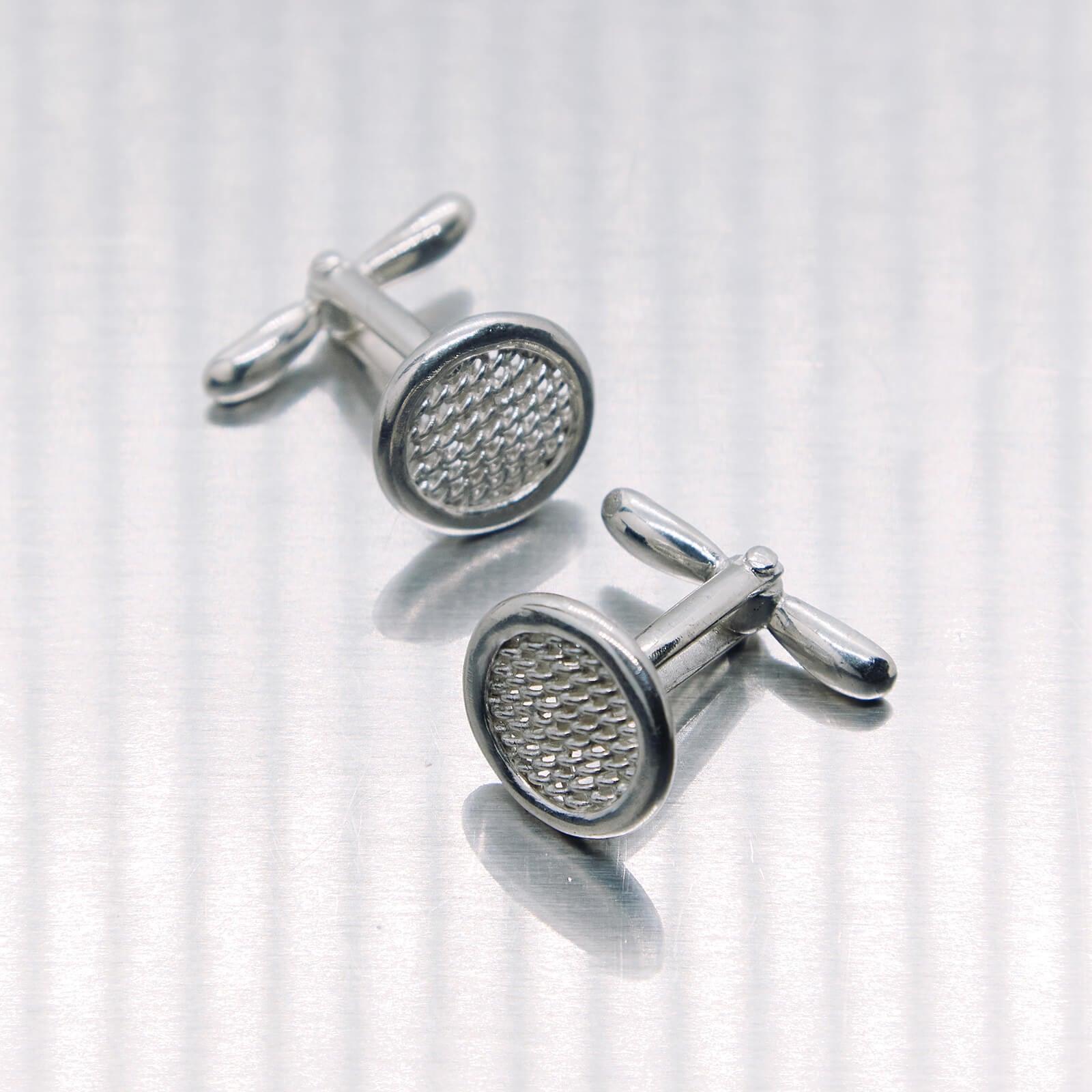 Silver cufflinks with textured design on a white background