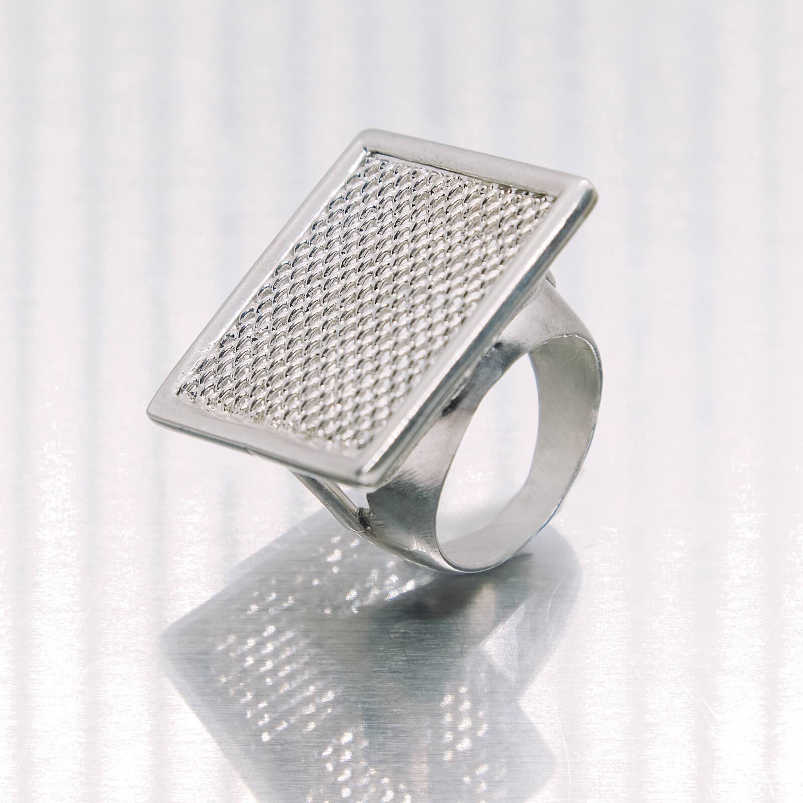 Silver ring with textured square design on a white background