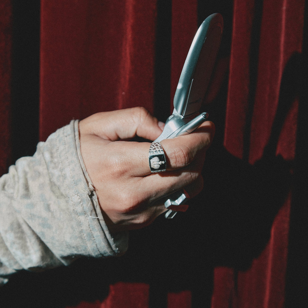 Hand holding a phone against a red curtain background with silver rings 