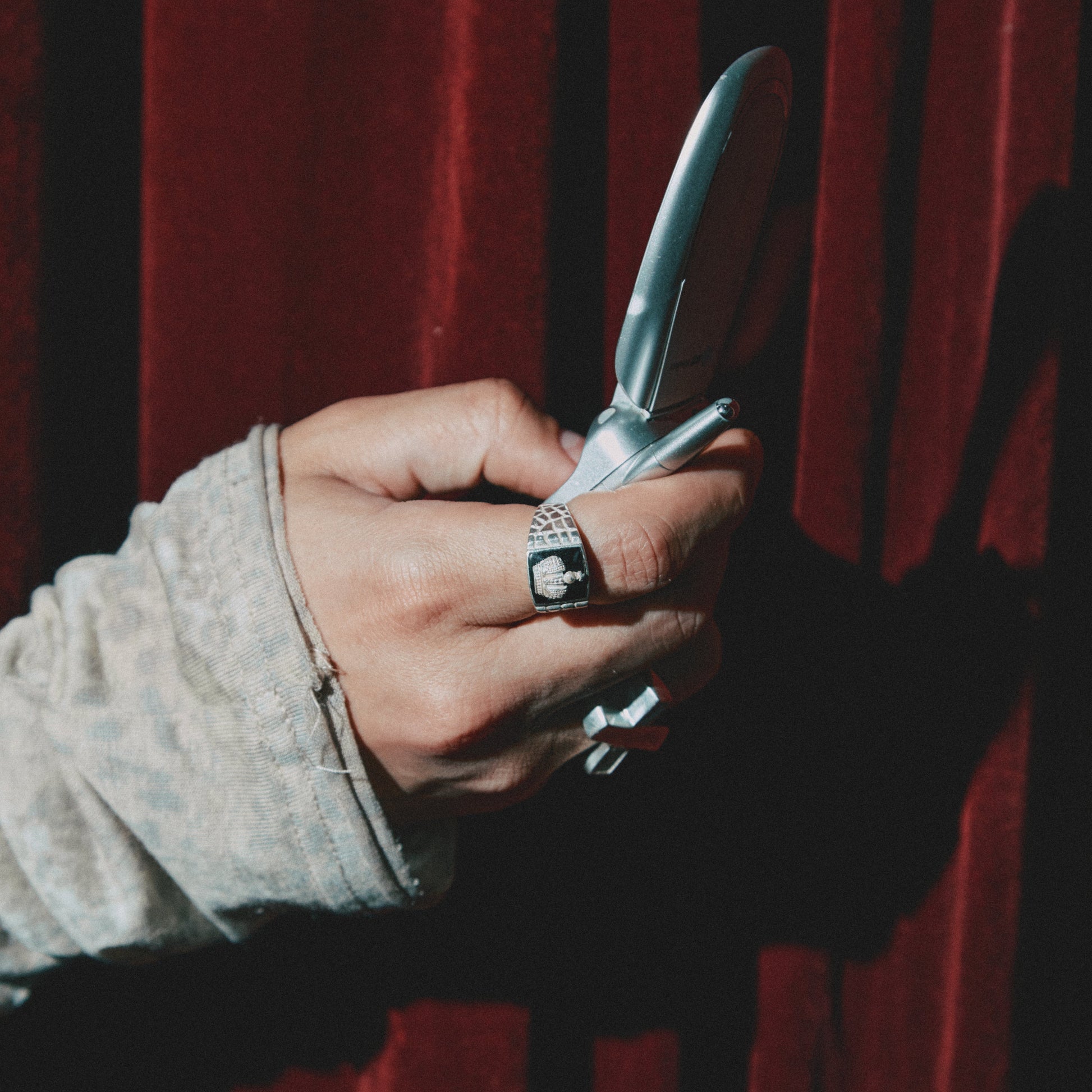 Hand holding a phone against a red curtain background with silver rings 